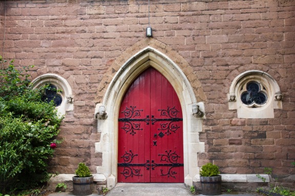 The, large, solid, rather imposing; main door of St. John's Church, Ladywood. It is flanked by carvings on either side.
